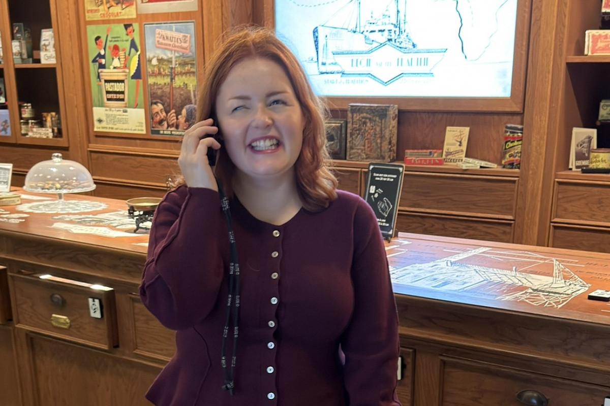 Woman smiles while talking on the phone in a shop with a wooden counter, vintage posters and an old rotary phone.